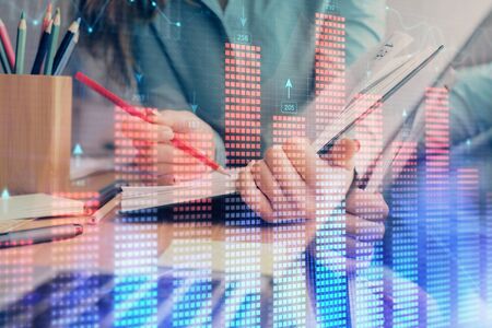 A woman hands writing information about stock market in notepad. Forex chart holograms in front. Concept of research. Multi exposureの写真素材