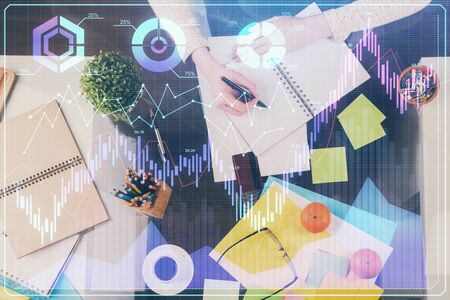 Hand taking notes in notepad. Forex chart holograms in front. Concept of research. Double exposureの写真素材