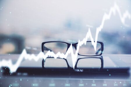 Financial graph hologram with glasses on the table background. Concept of business. Double exposure.