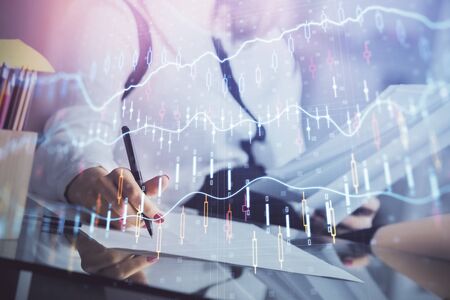 A woman hands writing information about stock market in notepad. Forex chart holograms in front....