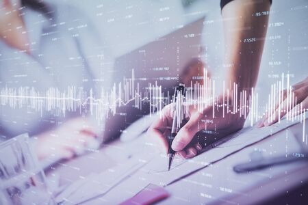 A woman hands writing information about stock market in notepad. Forex chart holograms in front....