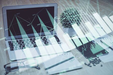 Stock market graph on background with desk and personal computer. Multi exposure. Concept of financial analysis.の写真素材