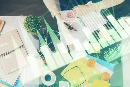 Hand taking notes in notepad. Forex chart holograms in front. Concept of research. Double exposureの写真素材