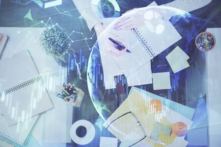 Hand taking notes in notepad. Forex chart holograms in front. Concept of research. Double exposureの写真素材