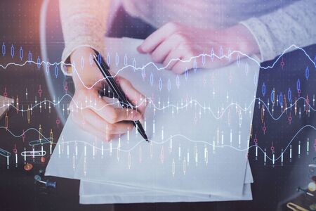Hands macking notes in notepad. Forex chart holograms in front. Concept of research. Multi exposureの写真素材