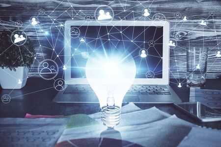 Computer on desktop in office with bulb icon hologram. Multi exposure. Concept of idea.の写真素材