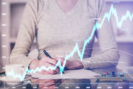 Hand taking notes in notepad. Forex chart holograms in front. Concept of research. Double exposureの写真素材