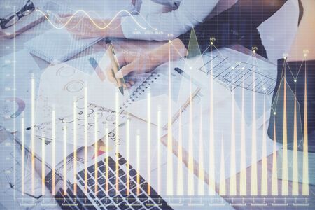 A woman hands writing information about stock market in notepad. Forex chart holograms in front. Concept of research. Double exposureの写真素材