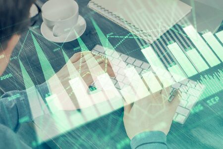 Double exposure of graph with man typing on computer in office on background. Concept of hard work.の写真素材