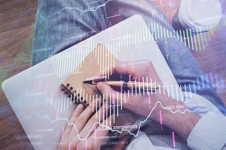 Double exposure of man doing notes of stock market with forex graph. Top View. Concept of research and trading.の写真素材