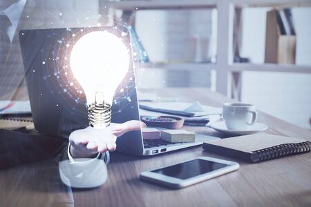 Computer on desktop in office with bulb icon hologram. Multi exposure. Concept of idea.の写真素材