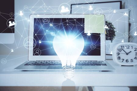Computer on desktop in office with bulb icon hologram. Multi exposure. Concept of idea.