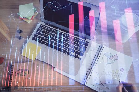 Double exposure of mans hands writing notes with laptop of stock market with forex graph background. Top View. Concept of research and trading.の写真素材