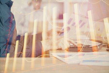 Double exposure of graph with man typing on computer in office on background. Concept of hard work. Closeup.の写真素材