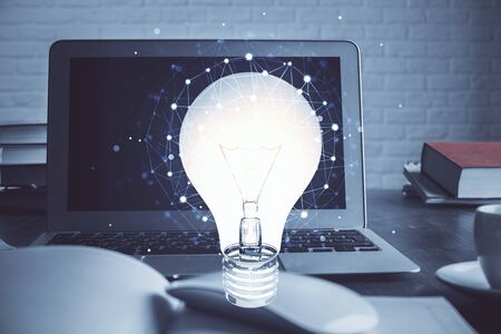 Computer on desktop in office with bulb icon hologram. Multi exposure. Concept of idea.の写真素材
