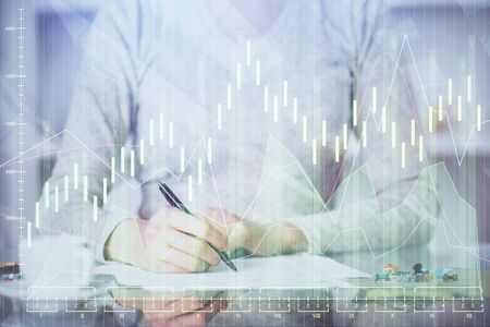 Hand taking notes in notepad. Forex chart holograms in front. Concept of research. Double exposure