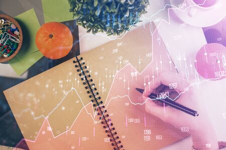 Forex chart hologram on hand taking notes background. Concept of analysis. Double exposureの写真素材