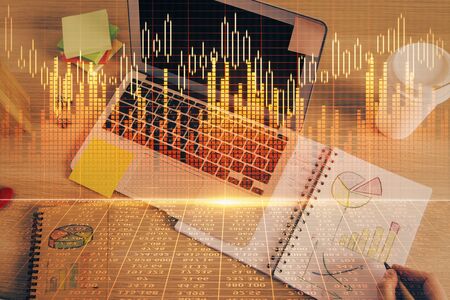 Double exposure of mans hands writing notes with laptop of stock market with forex graph background. Top View. Concept of research and trading.の写真素材