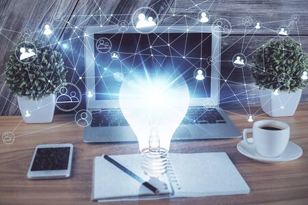 Computer on desktop in office with bulb icon hologram. Multi exposure. Concept of idea.の写真素材