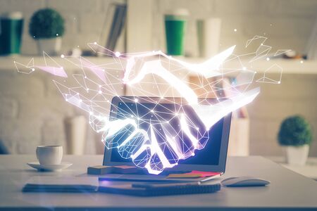 Desktop computer background in office and handshake hologram drawing. Double exposure. Pertnership concept.の写真素材