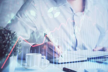 Double exposure of mans hands writing notes of stock market with forex graph background. Concept of research and trading.の写真素材