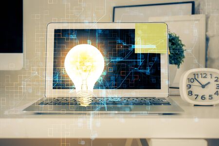 Computer on desktop in office with bulb icon hologram. Multi exposure. Concept of idea.の写真素材