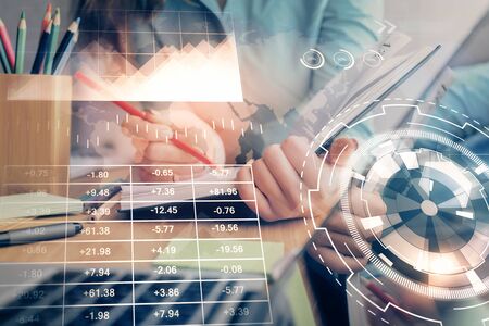 A woman hands writing information about stock market in notepad. Forex chart holograms in front....