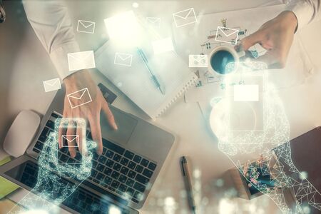 Double exposure of mans hands typing over computer keyboard and flying envelop hologram drawing. Top...