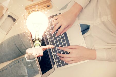 Double exposure of woman hands working on computer and light bulb hologram drawing. Top View. Idea concept.の写真素材