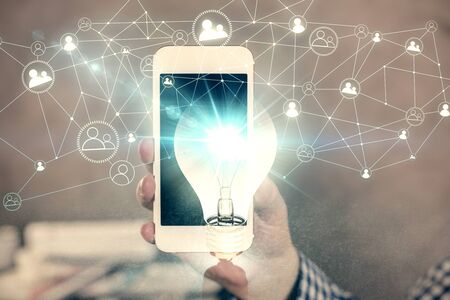 Double exposure of man's hands holding and using a digital device and bulb hologram drawing. Idea...