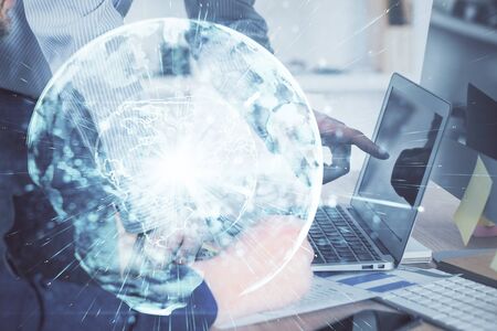 Double exposure of businessman working on laptop on background. International business hologram in front. Concept of success.の写真素材