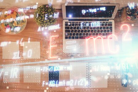 Physics and math theme hologram with formula drawings over computer on the desktop background. Top...