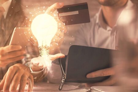Double exposure of man and woman on-line shopping holding a credit card and light bulb hologram drawing. Idea concept.の写真素材