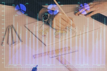 Double exposure of man's hands writing notes of stock market with forex graph background. Concept of research and trading.の写真素材
