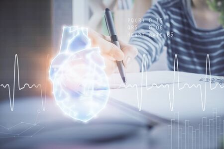Heart hologram over womans hands writing background. Concept of Medical study. Multi exposureの写真素材