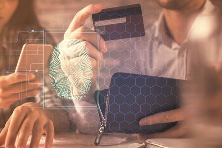 Double exposure of man and woman on-line shopping holding a credit card and fingerprint hologram drawing. Security in E-commerce concept.の写真素材