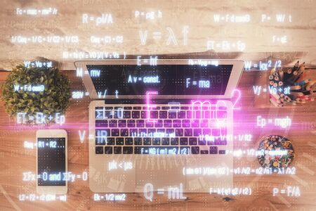Physics and math theme hologram with formula drawings over computer on the desktop background. Top...