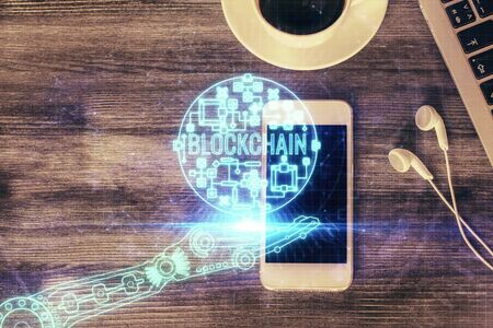 Double exposure of blockchain theme hologram over table with phone. Top view. Crypto technology...