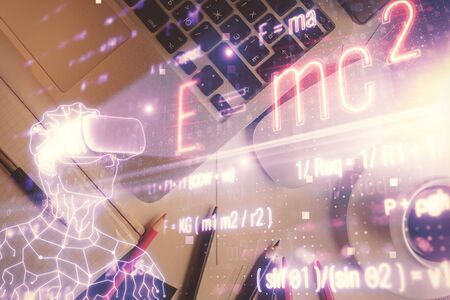 Physics and math theme hologram with formula drawings over computer on the desktop background. Top...