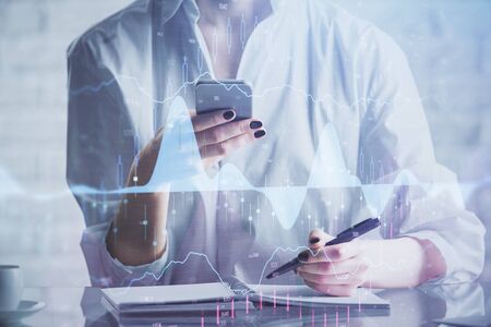 Double exposure of forex chart sketch hologram and woman holding and using a mobile device. Financial market concept.の写真素材