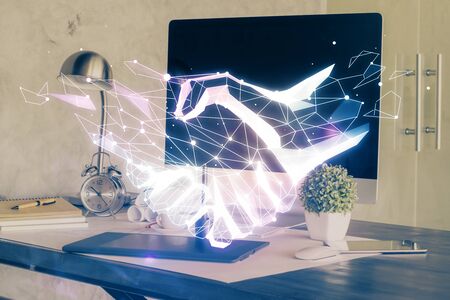 Desktop computer background in office and handshake hologram drawing. Double exposure. Pertnership concept.の写真素材