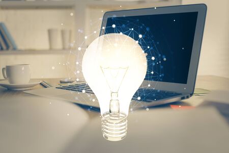 Computer on desktop in office with bulb icon hologram. Multi exposure. Concept of idea.の写真素材