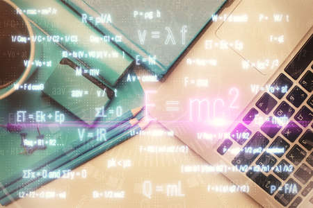 Physics and math theme hologram with formula drawings over computer on the desktop background. Top...