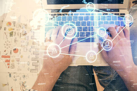 Double exposure of mans hands typing over computer keyboard and social network theme hologram...