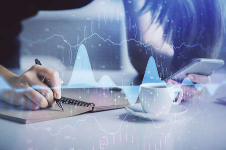 Double exposure of forex graph sketch hologram and woman holding and using a mobile device. Stock...