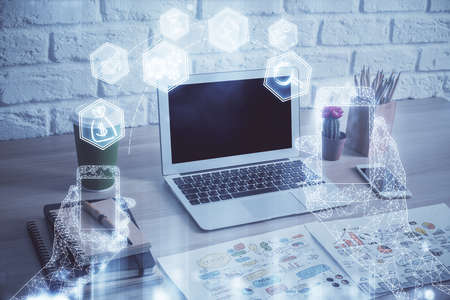 Computer on desktop in office with technology theme hologram. Double exposure. Tech concept.