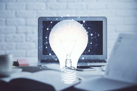 Computer on desktop in office with bulb icon hologram. Double exposure. Concept of idea.の写真素材