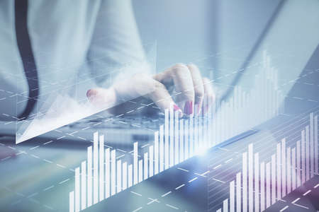 Double exposure of businesswoman hands typing on computer and financial graph hologram drawing....