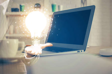 Computer on desktop in office with bulb icon hologram. Multi exposure. Concept of idea.の写真素材
