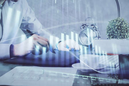 Double exposure of mans hands holding and using a phone and financial graph drawing. Analysis...
